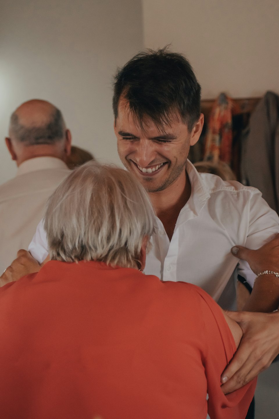 Man smiles while hugging an elderly person with grey hair.