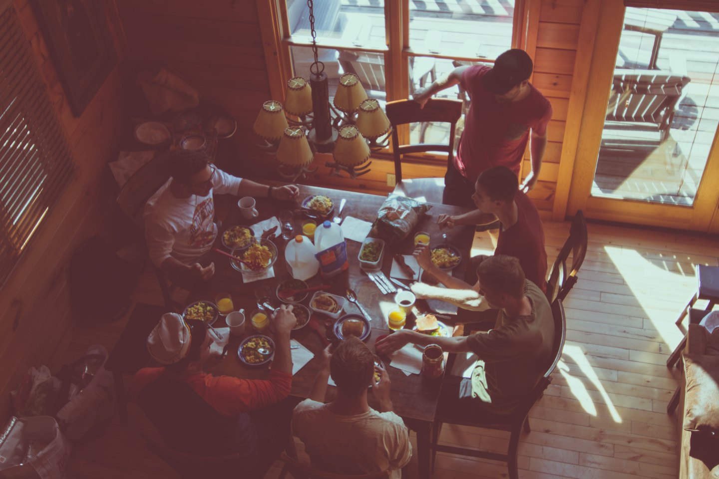 Young men enjoy a communal breakfast at a rustic wooden table.